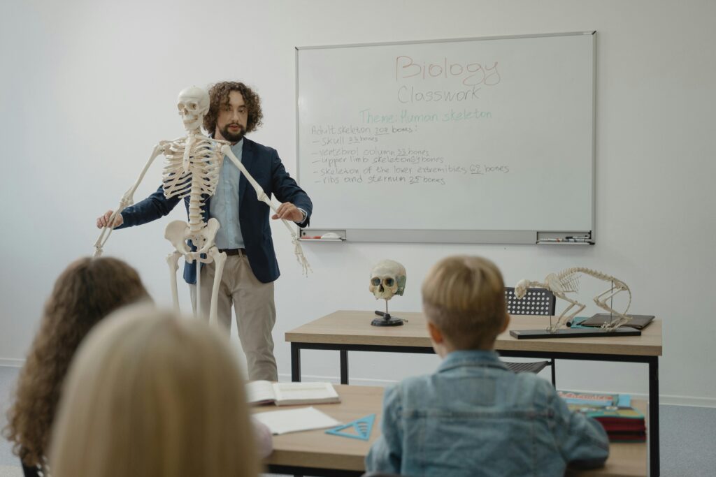 pexels-photo-5427819-5427819 Teacher explaining human skeleton to students in a biology class with models.